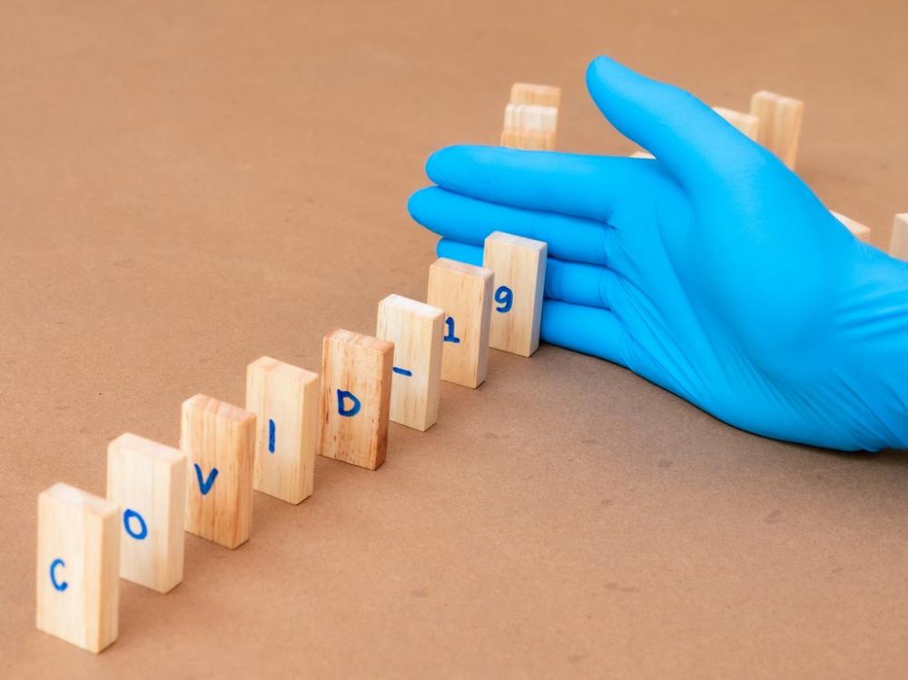 gloved hands keeps wood blocks reading COVID-19 from falling