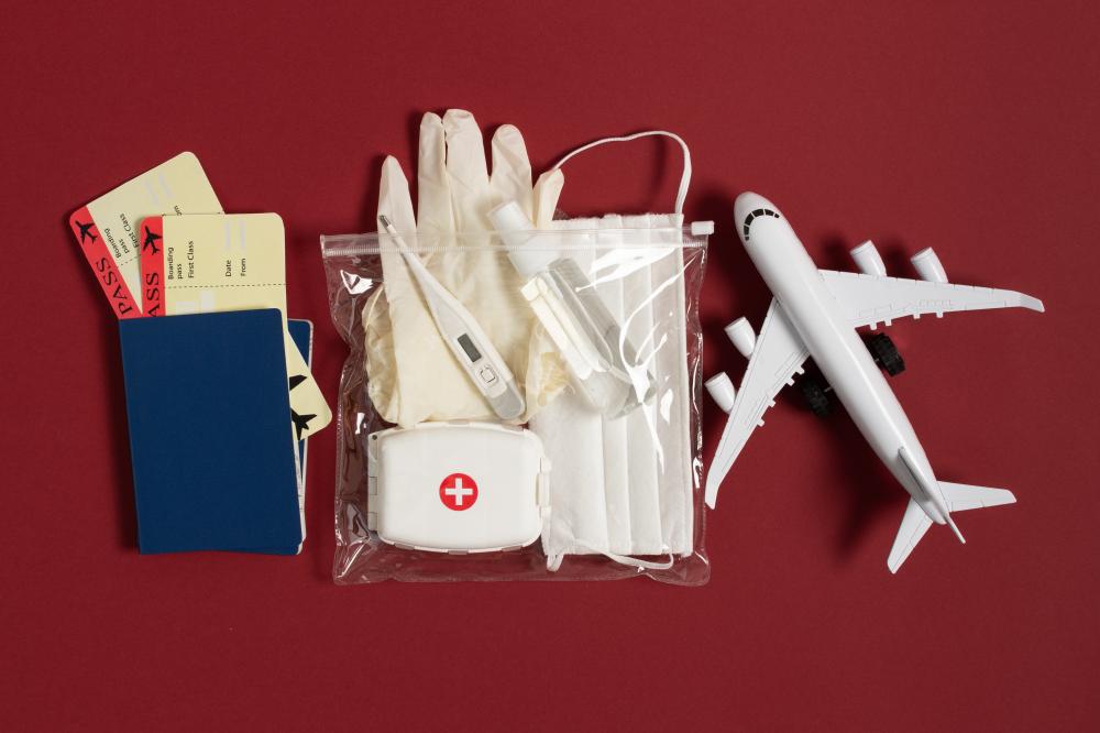 Passport and boarding pass with surgical mask, alcohol antiseptic gel and thermometer on dark red background top view.