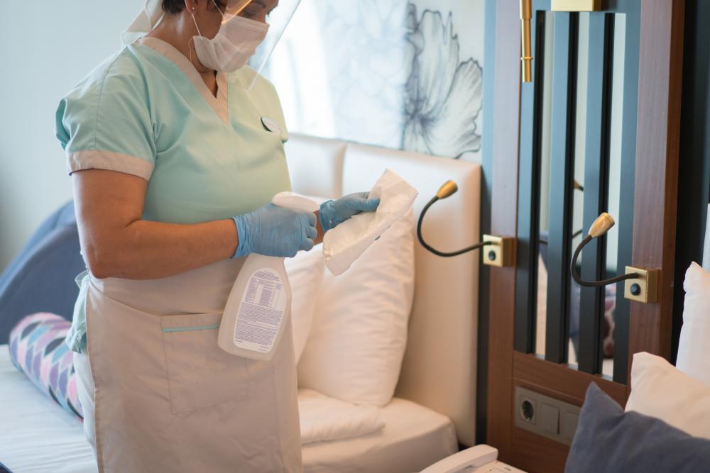 Female maid with medical mask cleaning a hotel room