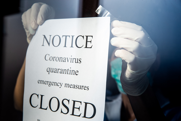 employee wearing gloves attaches a notice of closure to glass window
