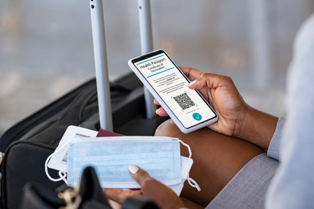 Close up of black hands of woman sitting in airport lounge checking her valid digital vaccination passport for covid19 while holding face mask and boarding pass