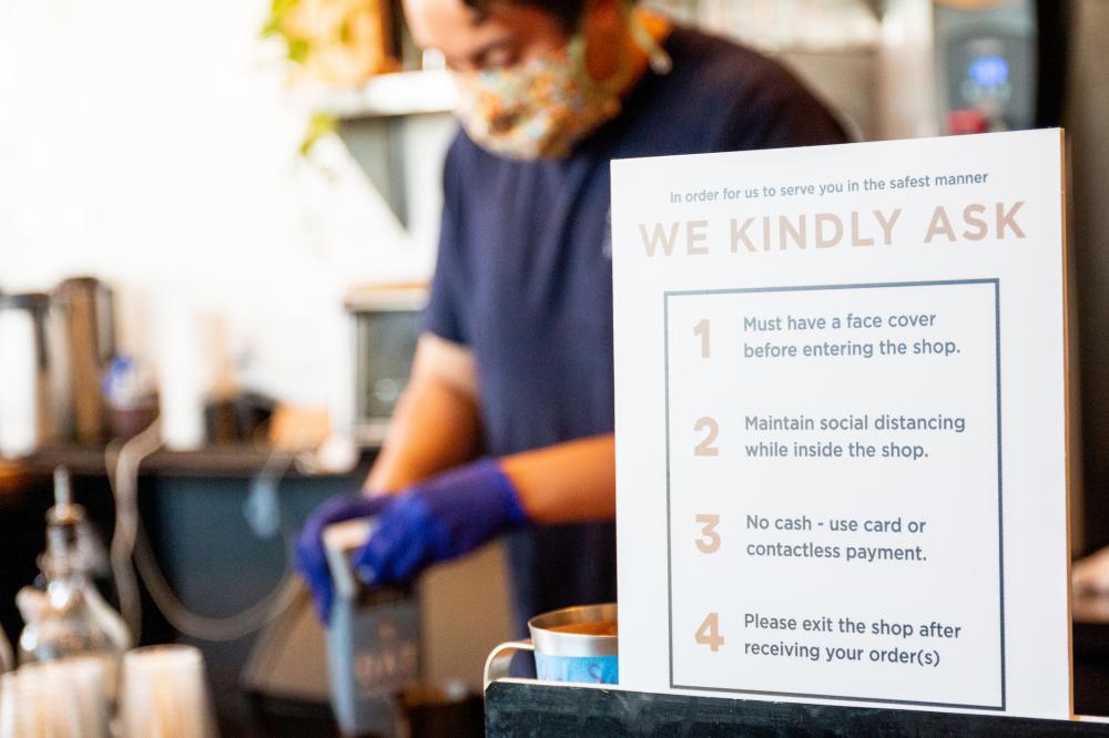 Man working in a coffee shop wearing a mask in background; list of safety actions for restaurant in foreground
