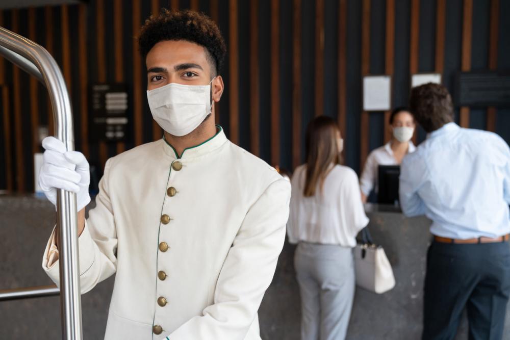Portrait of a happy bellboy working at a hotel and wearing a facemask to avoid COVID-19