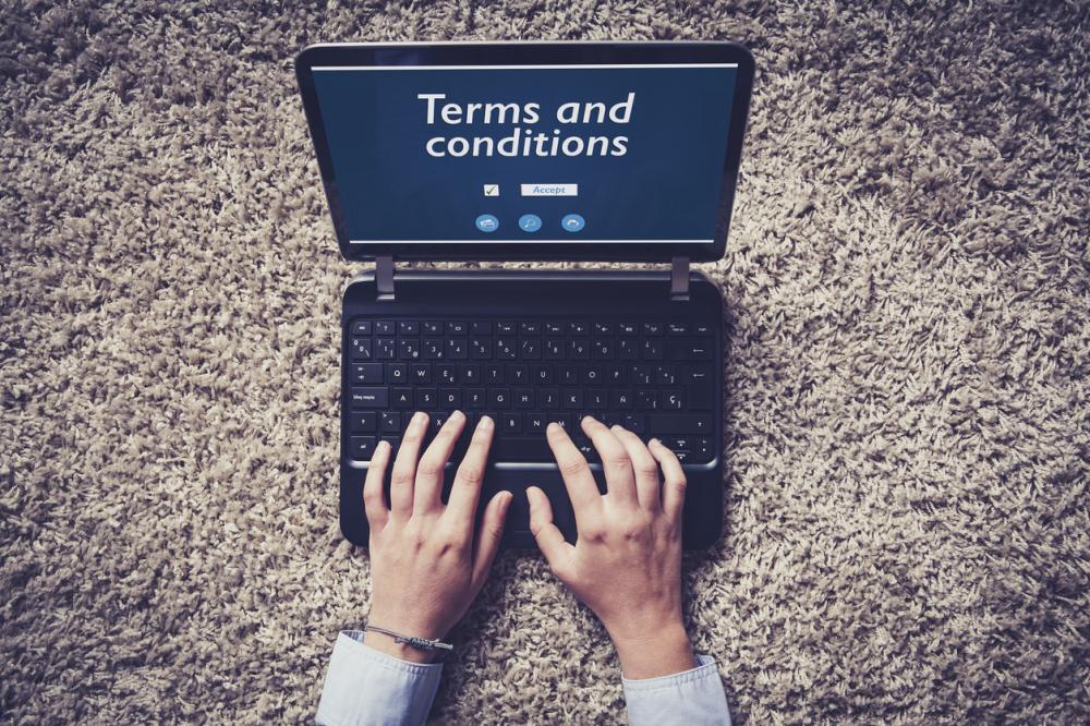 Woman hands typing on a laptop with terms and conditions text in the screen.