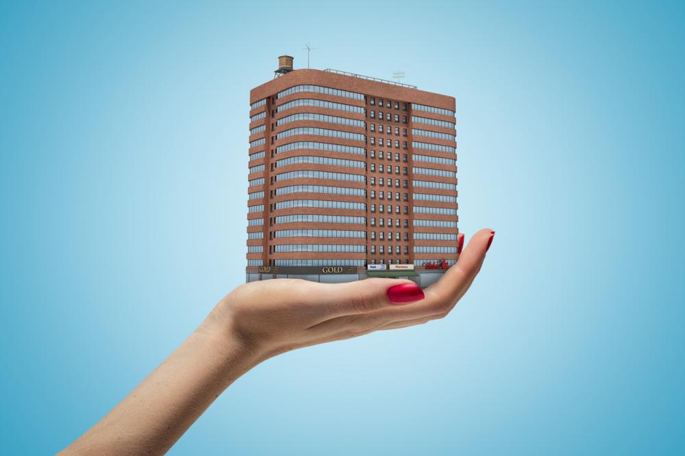 Side closeup of woman's hand facing up and holding multi-storey brick building on light blue background